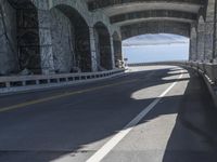 a couple of cars driving under an overpass on a bridge with large windows and a wall