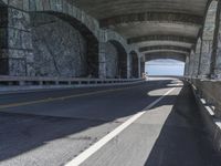 a couple of cars driving under an overpass on a bridge with large windows and a wall