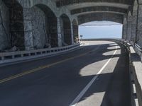 a couple of cars driving under an overpass on a bridge with large windows and a wall