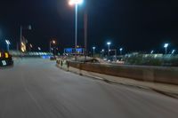 cars driving on the side of the road at night, passing lights and traffic posts