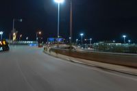 cars driving on the side of the road at night, passing lights and traffic posts