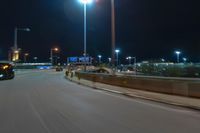 cars driving on the side of the road at night, passing lights and traffic posts