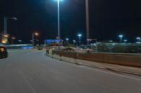 cars driving on the side of the road at night, passing lights and traffic posts