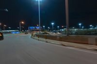 cars driving on the side of the road at night, passing lights and traffic posts