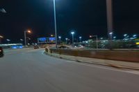 cars driving on the side of the road at night, passing lights and traffic posts