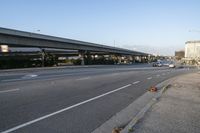 cars driving on the road in an intersection with an overpass and several tall buildings