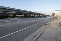 cars driving on the road in an intersection with an overpass and several tall buildings