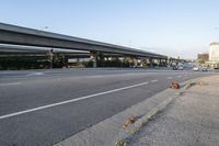 cars driving on the road in an intersection with an overpass and several tall buildings