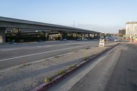 cars driving on the road in an intersection with an overpass and several tall buildings