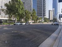 cars are driving down the street near tall buildings in a city, with the cars parked on the curb