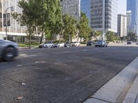 cars are driving down the street near tall buildings in a city, with the cars parked on the curb