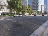 cars are driving down the street near tall buildings in a city, with the cars parked on the curb