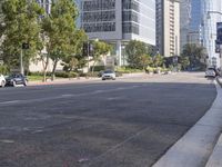 cars are driving down the street near tall buildings in a city, with the cars parked on the curb