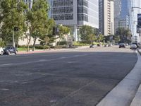 cars are driving down the street near tall buildings in a city, with the cars parked on the curb