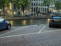 cars parked next to the water on a brick road near buildings and a street lamp