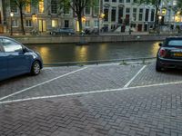 cars parked next to the water on a brick road near buildings and a street lamp