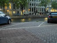 cars parked next to the water on a brick road near buildings and a street lamp