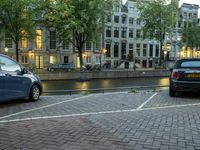 cars parked next to the water on a brick road near buildings and a street lamp