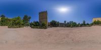 the sun shining over a castle in the desert with some trees and bushes around it