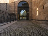 a cat that is sitting on the ground of a walkway near a building with an arched doorway