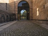 a cat that is sitting on the ground of a walkway near a building with an arched doorway