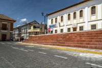 an empty road on the side of a large white building near a street with stairs