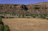 there is a person walking across a dirt field by the mountains on a sunny day