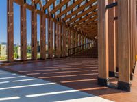 the underside beams of an outdoor wood pavilion structure overlooking water and hills with trees and grass