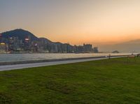 the large grassy area is next to the beach in front of the city skyline with mountains and trees