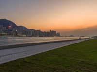 the large grassy area is next to the beach in front of the city skyline with mountains and trees