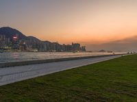 the large grassy area is next to the beach in front of the city skyline with mountains and trees