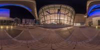 the building looks like it is inside of a circle of buildings at night time with its own reflection in a circular