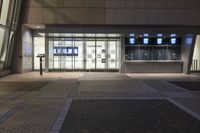 an empty, illuminated building at night with a large glass front door and windows with television screens on each side