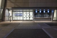 an empty, illuminated building at night with a large glass front door and windows with television screens on each side