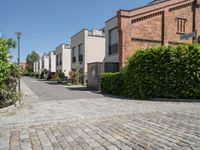 a paved sidewalk in a residential area with red brick walls, bushes, and street lights