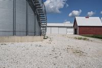 two barns that are sitting on gravel in a field next to some buildings and a silo