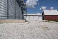 two barns that are sitting on gravel in a field next to some buildings and a silo