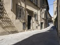 a narrow street in the shade of old buildings, with many windows, casting shadows on it