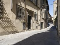 a narrow street in the shade of old buildings, with many windows, casting shadows on it