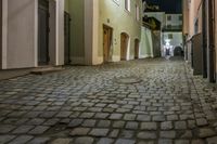 cobbled walkway in an old narrow alley leading to tall buildings at night time,