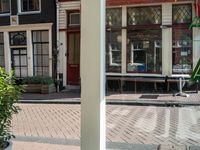 an image of a sidewalk with a table and chair near it and a plant on the right side