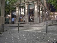 there are a lot of trees in the street outside the shops window at night,