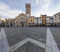 a view of a town square with a tower in the background and stone pathways around it