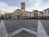 a view of a town square with a tower in the background and stone pathways around it