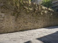 a stone wall beside a pathway in an old city with a bicycle parked next to it