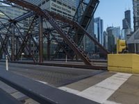 an outdoor bridge with a yellow bench in the middle and high buildings in the background