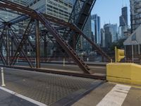 an outdoor bridge with a yellow bench in the middle and high buildings in the background