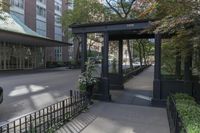 a small covered street next to a tall building with some flowers on the ground and a gated entrance