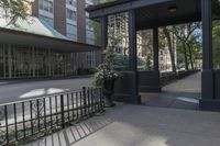 a small covered street next to a tall building with some flowers on the ground and a gated entrance