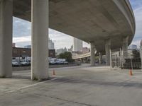 a parking lot with several concrete pillars next to buildings with cars parked under it and orange cones surrounding them